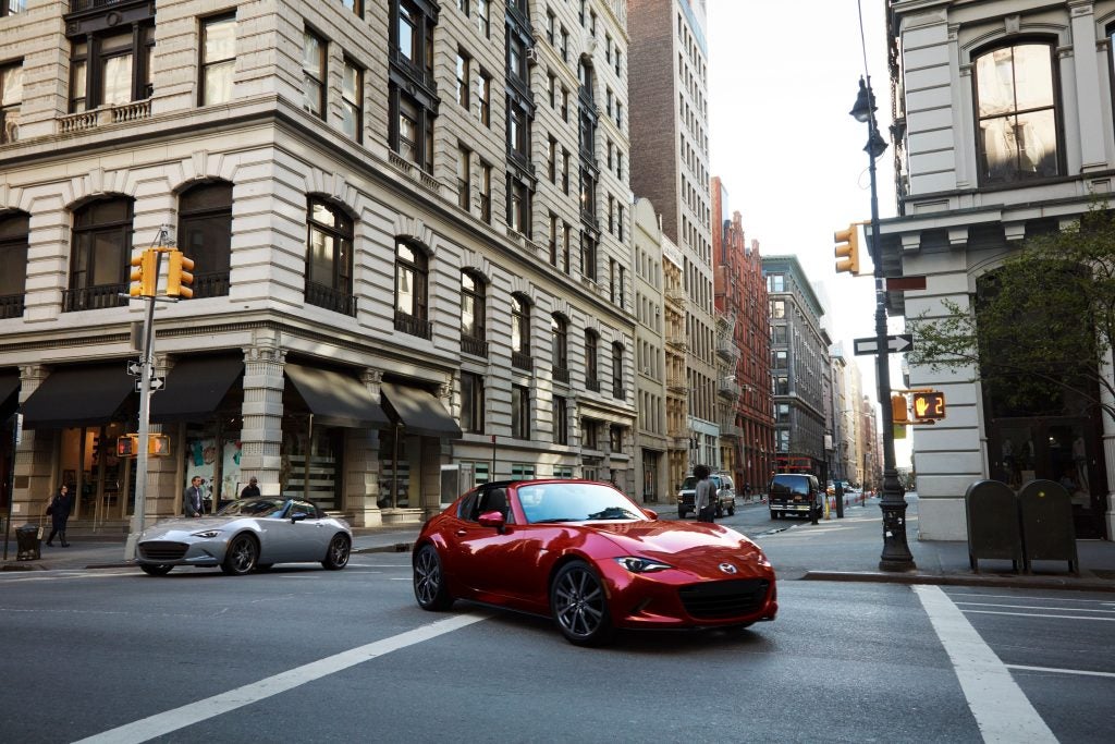 image of a cityscape with a red mazda miata front and center