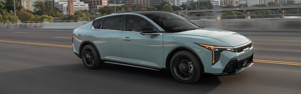 2026 Kia K4 sedan driving through a city road with modern exterior styling and urban background