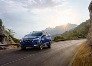 2022 Blue Chvy Equinox driving on a road with the sun behind it.
