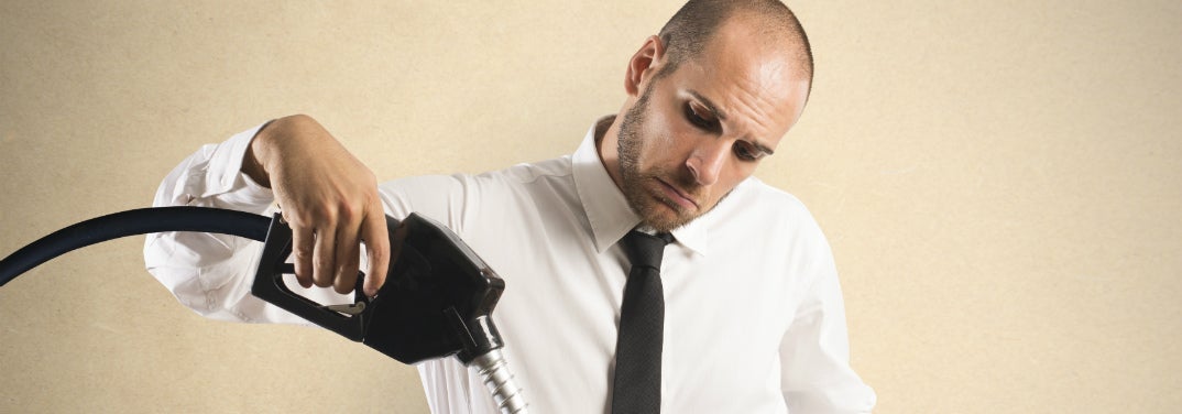 A man holds a gas hose indoors and looks perplexed.