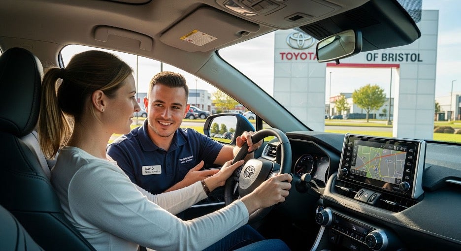 Customer test-driving a Toyota SUV near Toyota of Bristol dealership, with a sales advisor in the passenger seat and scenic Tennessee road ahead.