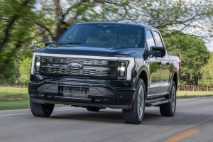 A black 2022 Ford F-150 Lighting driving on the backroad surrounded by trees.