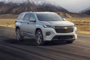 A silver 2022 Chevy Traverse driving on the highway with the snowcap mountains in the background.