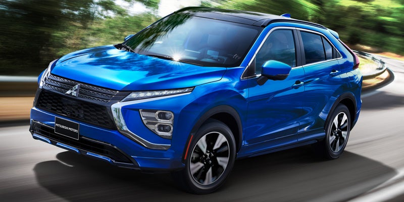 Blue Mitsubishi Eclipse Cross compact SUV driving curving right on a highway, green trees in background.