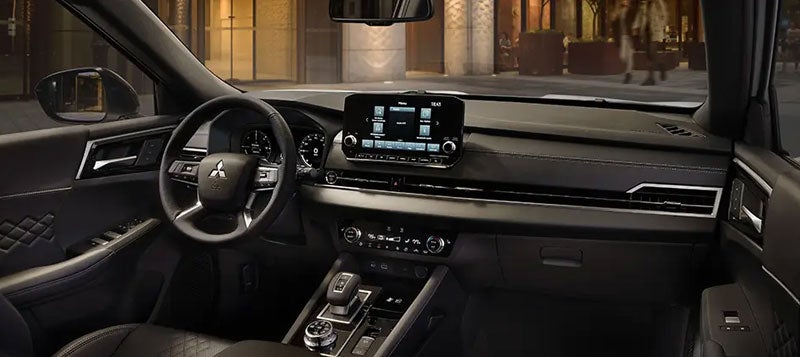 The dark interior of a car at night, featuring dashboard, steering wheel, infotainment screen, and gear shift.