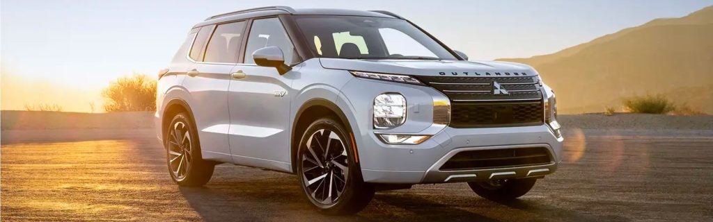 Light gray 2023 Mitsubishi Outlander PHEV SUV on an asphalt road with desert mountains in the background
