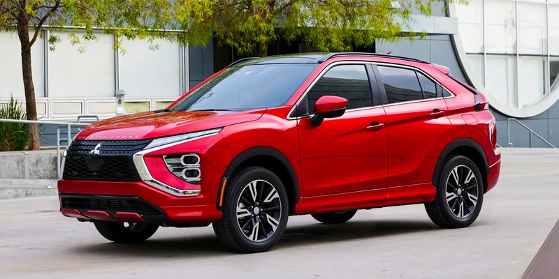 A bright red Mitsubishi Eclipse Cross SUV parked on a paved lot in front of a modern building with trees.