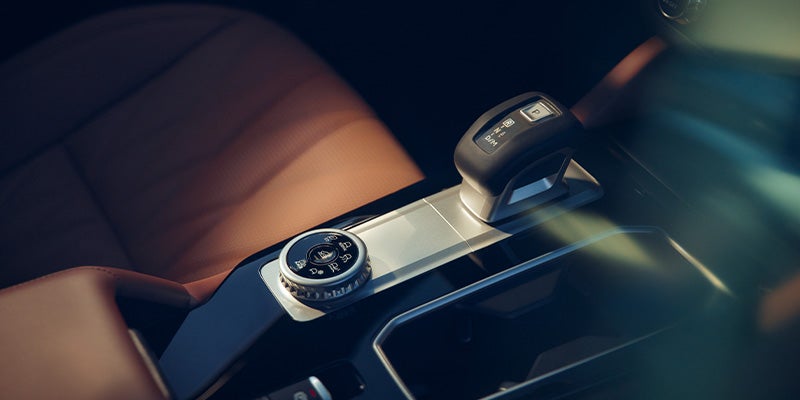 Close-up of a car's interior, showing the gear shifter, driving mode selector, and brown leather seats.