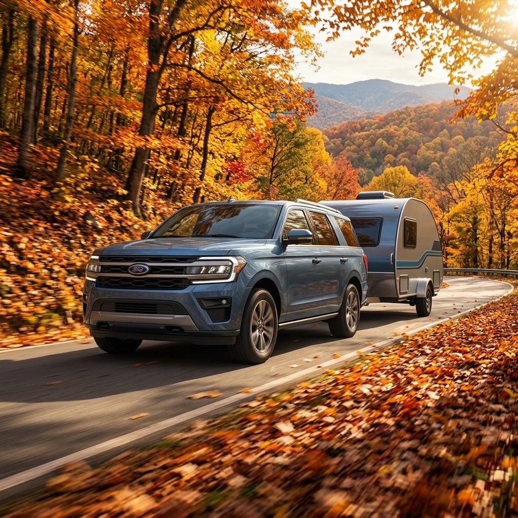 A blue SUV towing a teardrop camper trailer along a scenic road lined with vibrant autumn trees. (Representative image for illustration purposes only. Actual vehicle may vary based on trim and configuration.)