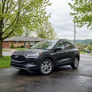 Cinematic outdoor shot, low-angle perspective, a clean 2026 Ford escape parked on a damp asphalt driveway of a modest mid-century ranch-style home in East Liverpool, Ohio, late spring afternoon, May 15, lush green budding maple trees, overcast sky with soft diffused light, realistic reflections on the truck’s wet metallic paint, the front wheel is turned to showcase the large brake rotor and caliper through the spokes of the rim, focus on the mechanical precision of the braking system, quiet residential street with power lines and a distant view of the Ohio River valley bluffs, temperate spring atmosphere, crisp details, natural color palette of slate grays and vibrant greens, family-oriented safety mood, professional photography style.