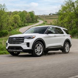 Photorealistic automotive photography of a pristine 2026 Ford Explorer with a high-gloss metallic finish, driving along a winding road through the gently rolling hills of the Ohio and Pennsylvania tri-state area, low-angle dynamic three-quarter view focusing on the clean rocker panels and polished wheels, spring
