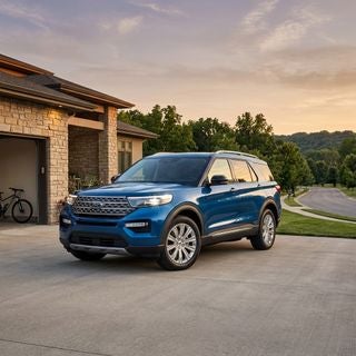 Automotive photography, a brand-new metallic blue Ford Explorer parked in the driveway of a contemporary stone-accented home, lush green trees and rolling hills typical of the American tri-state region in the background, low-angle hero shot, warm golden hour lighting, soft orange and purple sky, glinting chrome accents, polished paint reflecting the sunset, clean paved road, cinematic atmosphere, aspirational family lifestyle, sharp focus, hyper-realistic, rich textures, vibrant color palette, professional lighting, high contrast.
