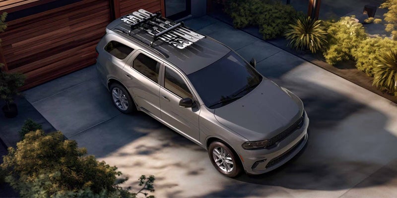 A silver SUV with skis loaded on its roof rack, parked on a paved driveway next to a wooden garage.