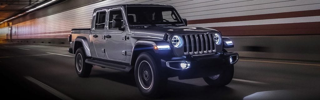 Gray Jeep Gladiator pickup truck driving through a tunnel with its headlights on.