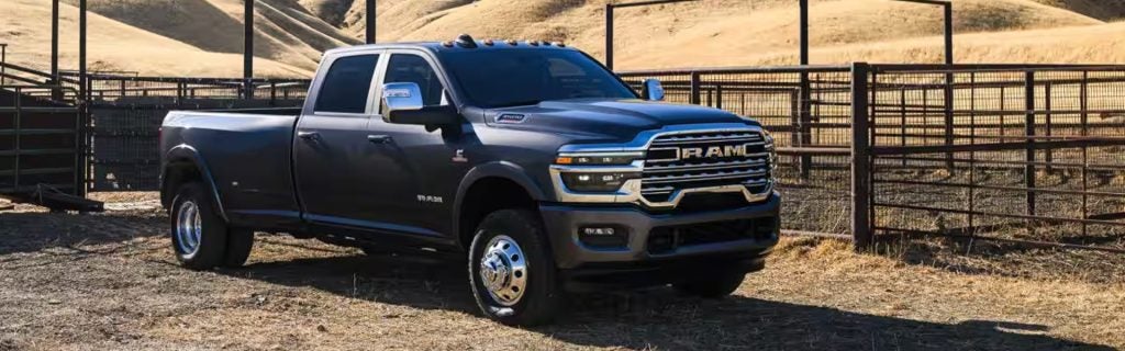 A dark gray RAM 3500 heavy-duty dually pickup truck parked next to a fenced corral on a ranch.