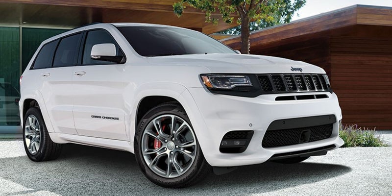 White Jeep Grand Cherokee SUV parked on a paved driveway with a modern house in the background.