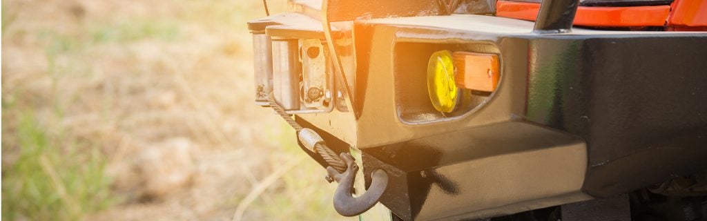 A heavy-duty black bumper with yellow turn signals and a tow hook with a wire rope attaches to a truck.