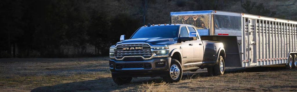 RAM Heavy Duty pickup truck towing a large livestock trailer, showcasing its powerful towing capability in a rural setting.
