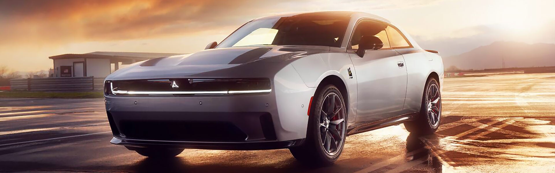 Silver Dodge Charger Daytona SRT on a wet asphalt track with a warm sunset sky.