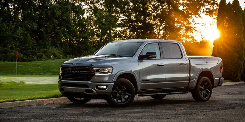 A grey Ram pickup truck parked on asphalt with a golf course in the background and a bright sunset.