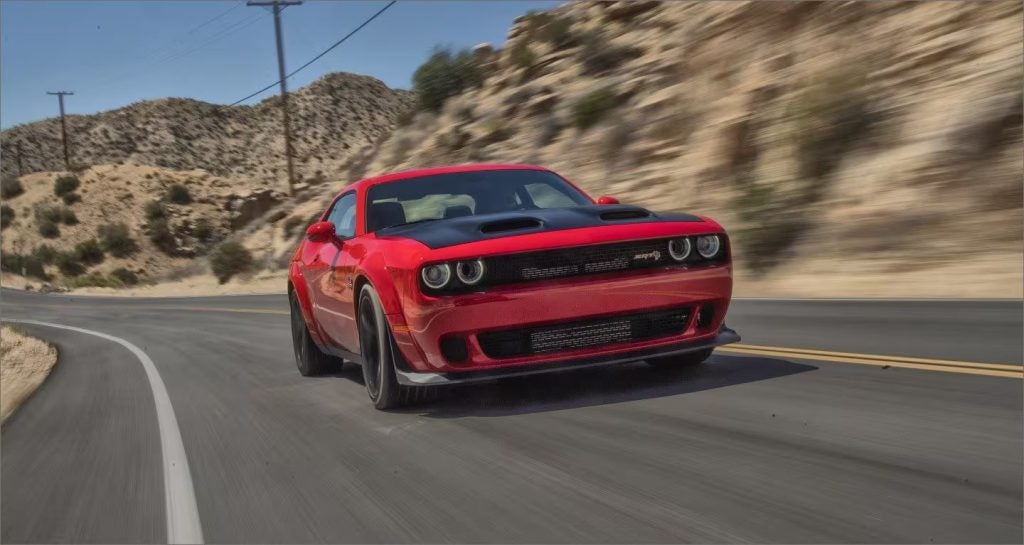 Red Dodge Challenger SRT Demon driving on a winding desert road with hills and power lines in the background.