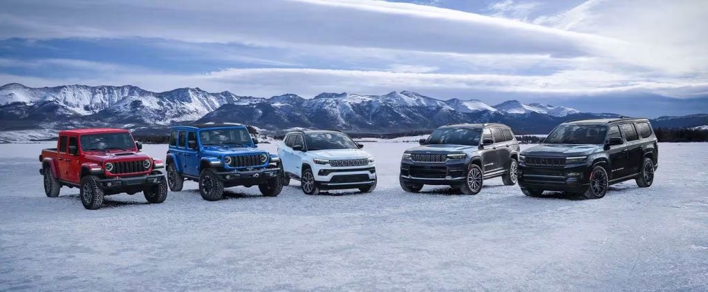 Five Jeep vehicles red Gladiator, blue Wrangler, white Compass, gray Grand Cherokee and black Wagoneer on snowy terrain with mountains.