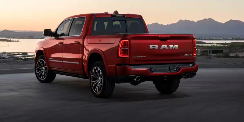 Rear view of a red Ram pickup truck with its backlights illuminated, parked by a lake, with mountains in the background.