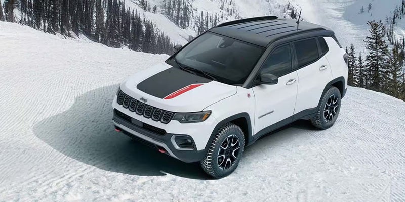 White Jeep Compass SUV with black roof and hood stripe, parked in a snowy mountain landscape.