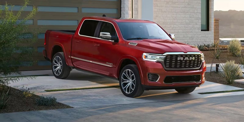 A red Dodge Ram parked on a driveway in front of a modern house, with desert plants in the foreground.