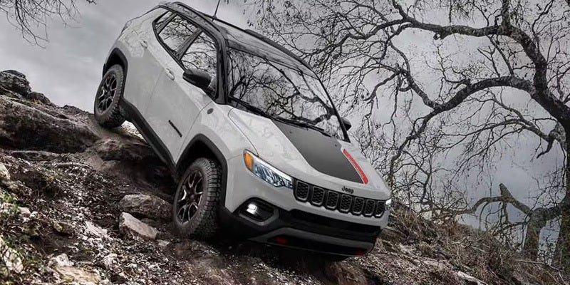 White Jeep Compass navigating a steep rocky off-road trail in rugged terrain.