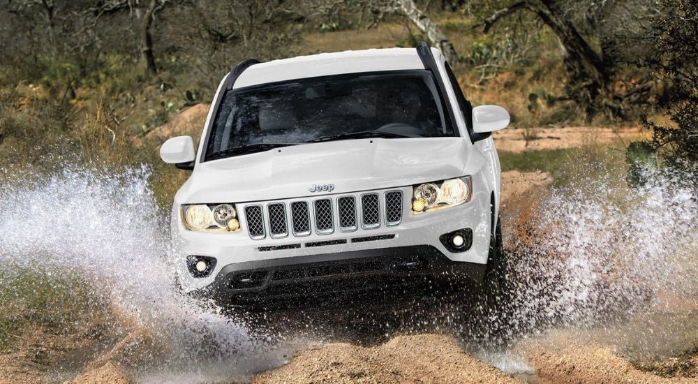 A white 2017 Jeep Compass is shown splashing through a creek after looking at used SUVs for sale.