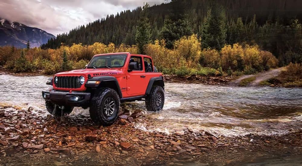 A red 2024 Jeep Wrangler Rubicon driving over a shallow river.