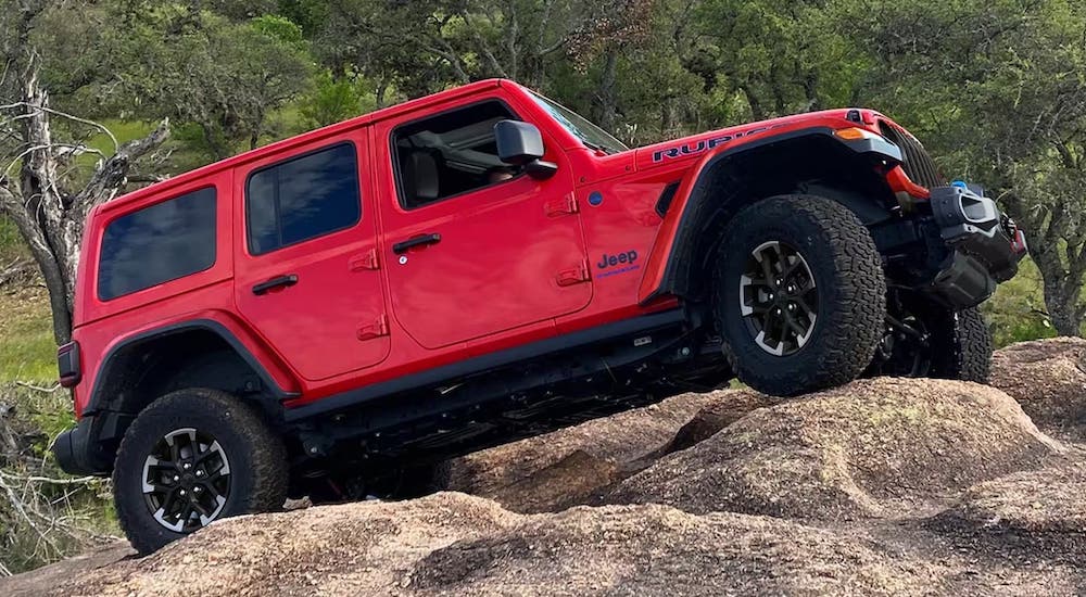 Side angle view of a red 2024 Jeep Wrangler driving over a boulder.