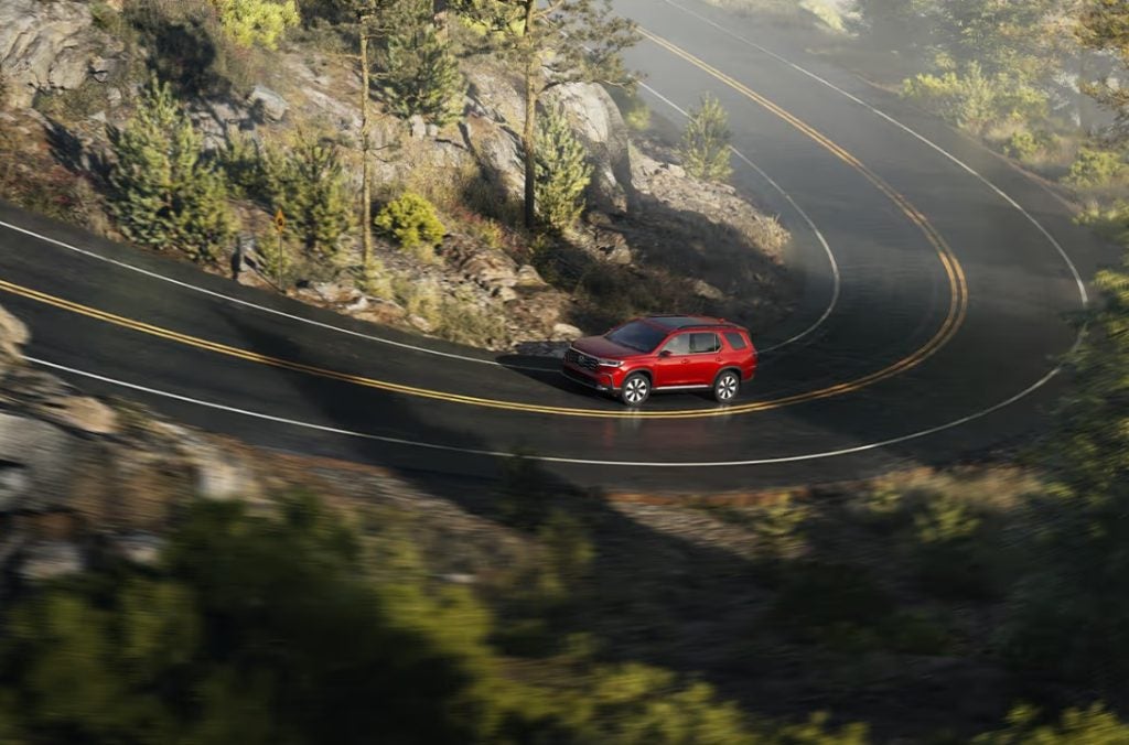 The new 2025 Honda Pilot is seen driving up around curved, mountainous roads. Shop for your new Pilot at Stonecrest Honda.