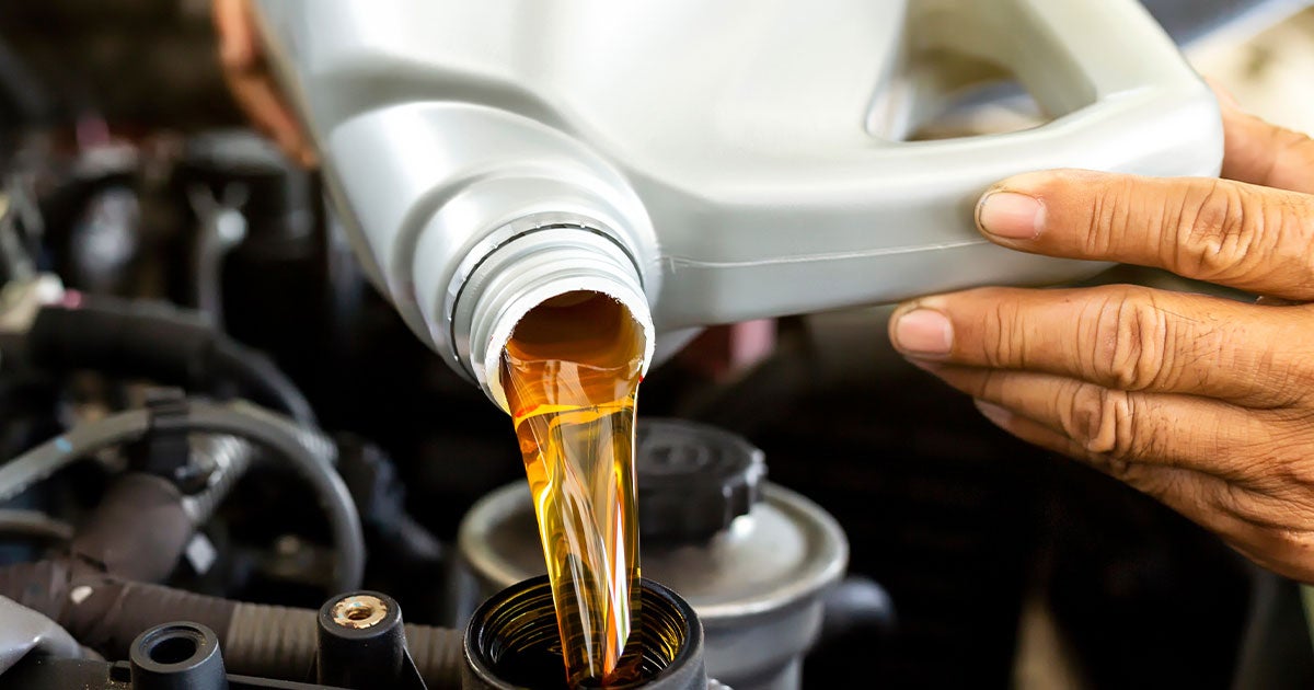 Close-up of a service technician refilling a vehicle's engine oil.