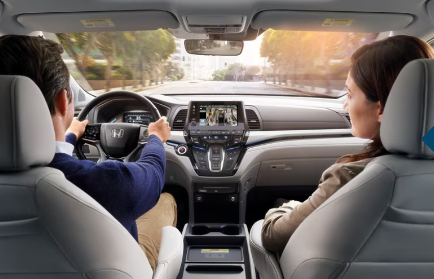 A couple drives a new Honda, showcasing the dashboard and safety features.