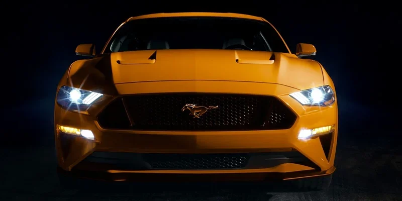 Front close up shot of a brand new bumble bee (transformers) yellow 2023 Ford Mustang with a dark, almost black, background. The car is the only item illuminated.