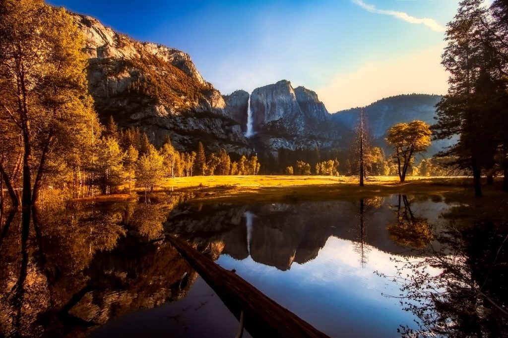 Landscape lake scene with a small mountain range in the background with sunset rays hitting the tree line to the left.