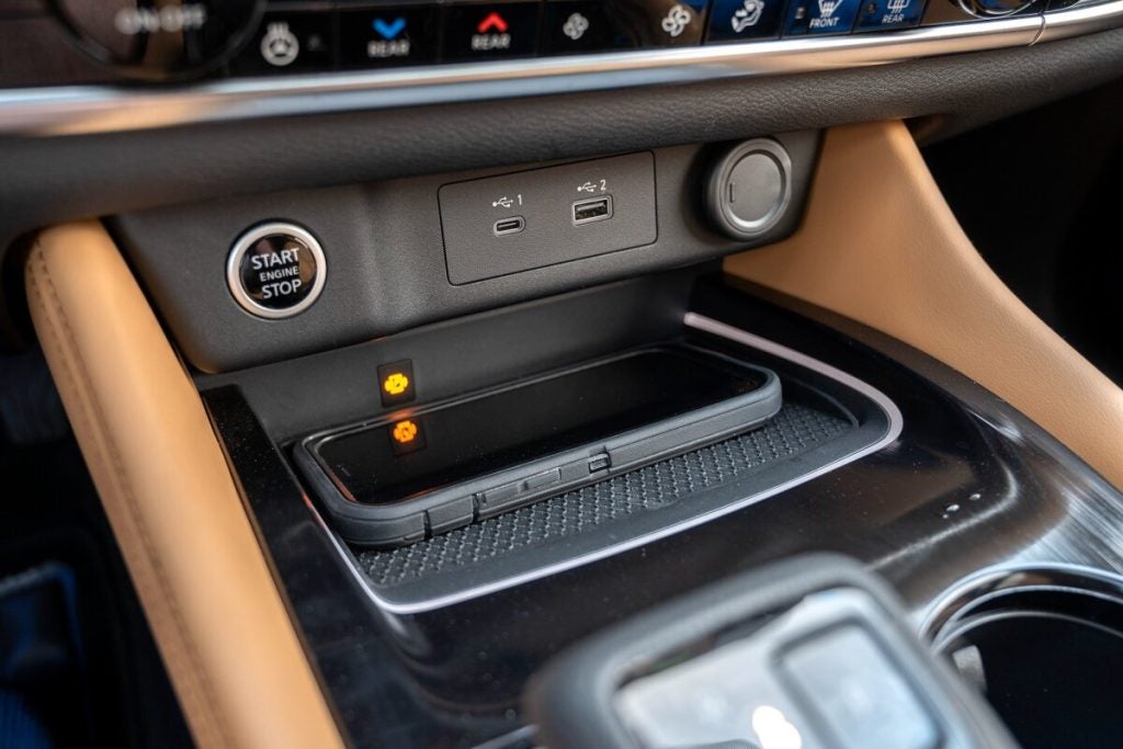 close up image of a cars start engine button with usb ports and a cell phone lying in the tray underneath 