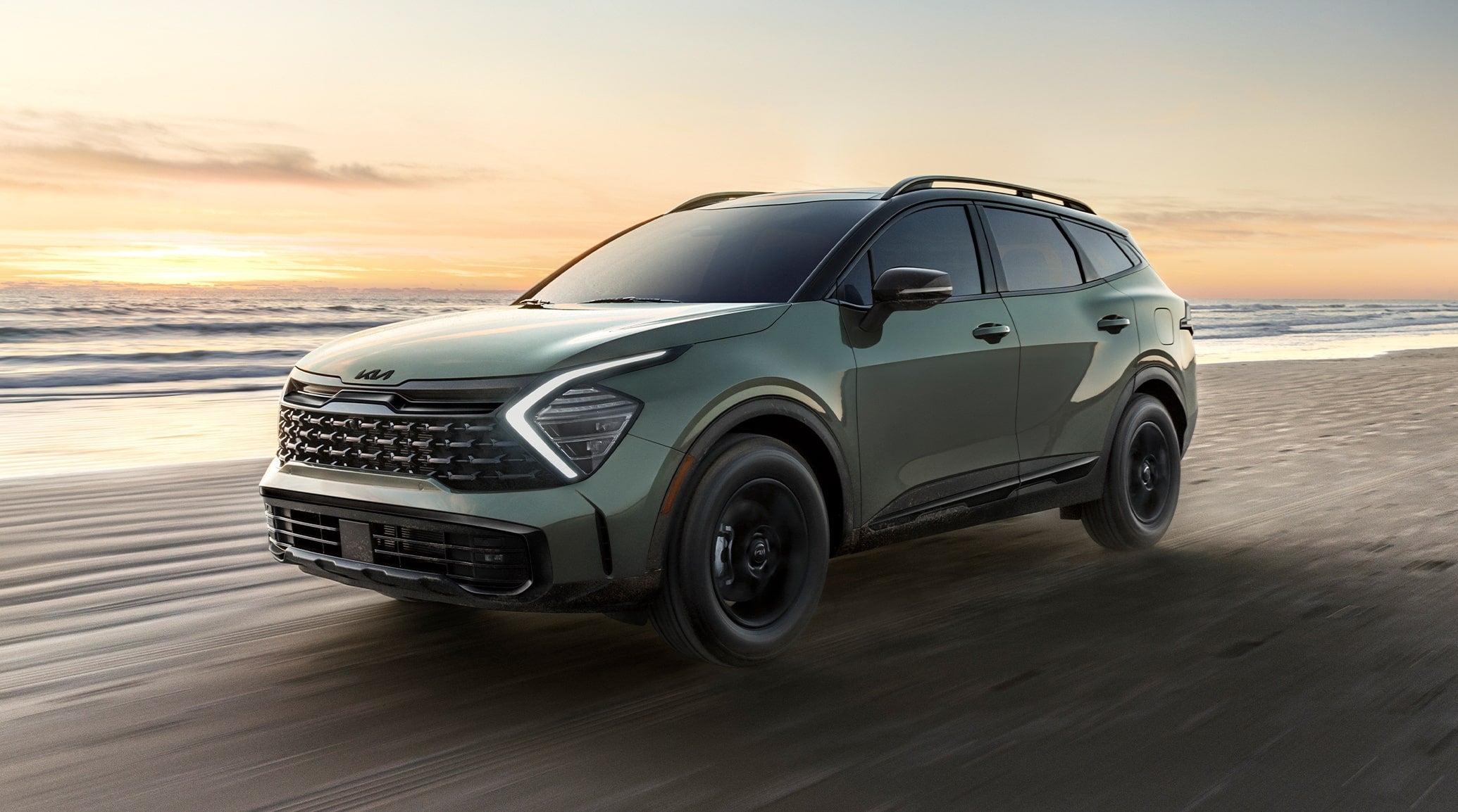 Green 2025 Kia Sportage SUV driving along a beach