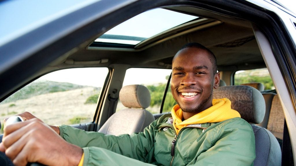 an african american man holding the wheel of a car while smiling at the camera 