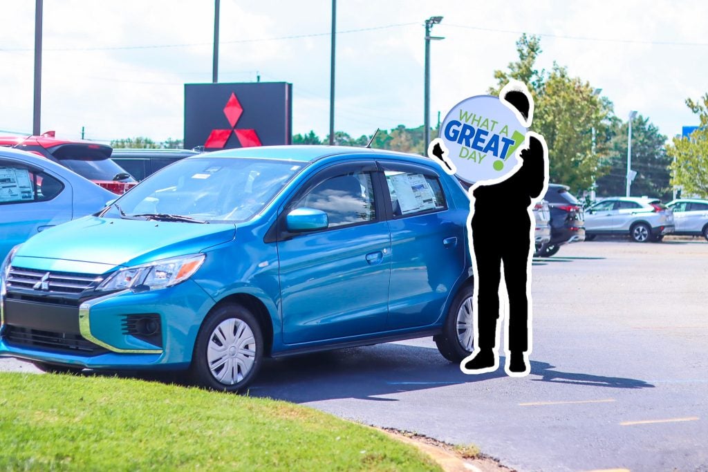 a person shaped sign holding a sign that says "what a great day!" next to a light blue hatchback 
