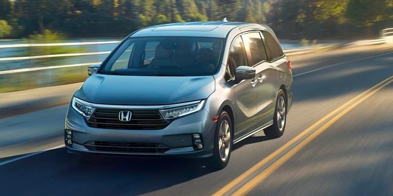 A photo of a gray Honda Odyssey driving down a street.