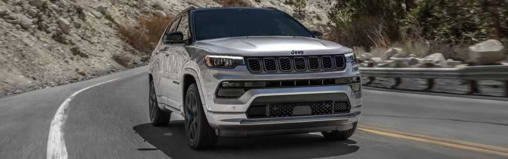 Silver Jeep Compass SUV driving on a mountain highway, front-side view.