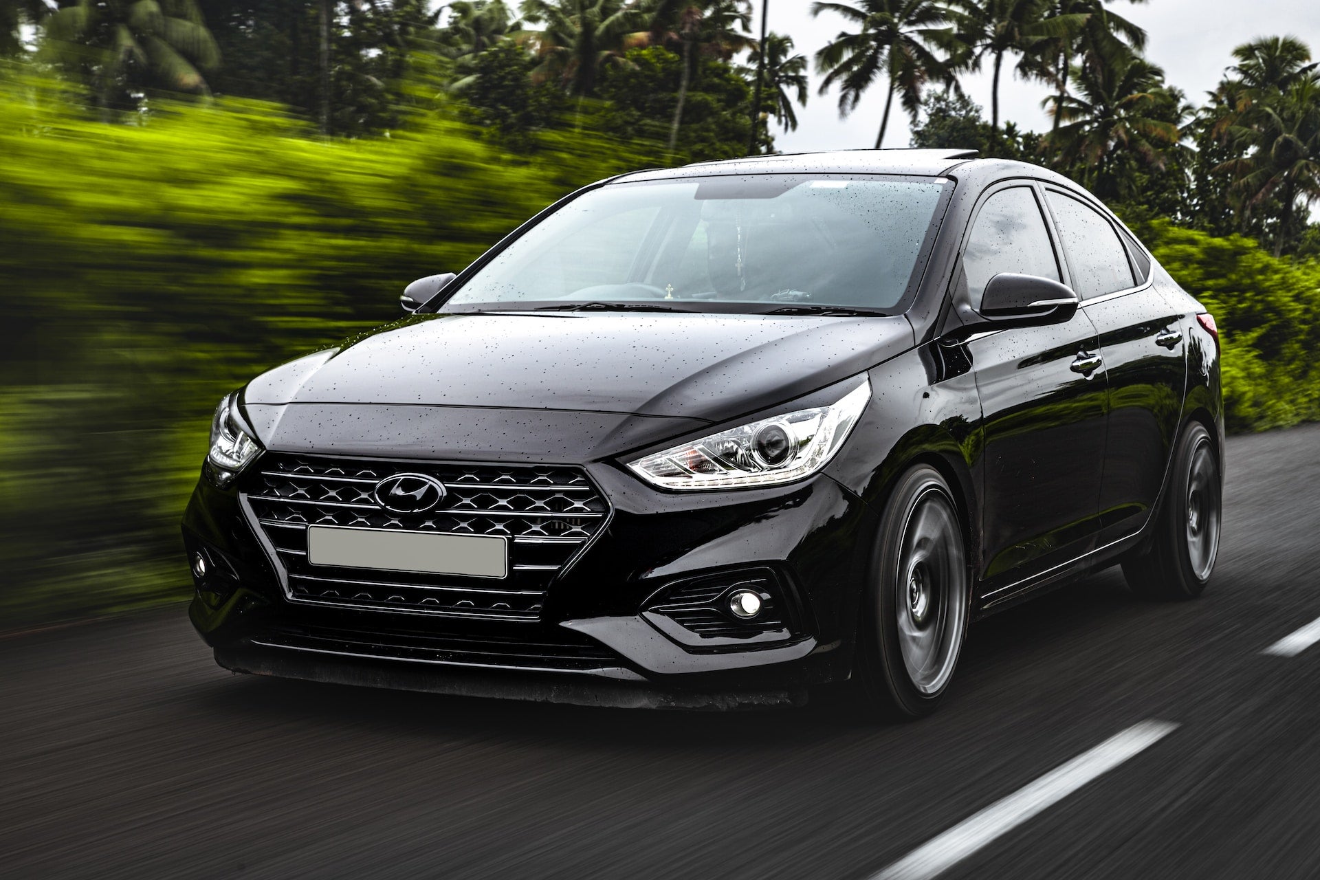 Black Hyundai driving fast down the road with trees behind it