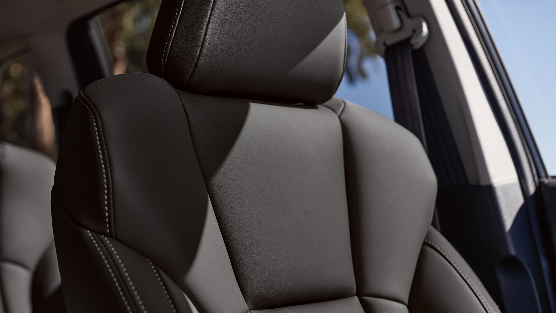 Close-up of a black leather car seat with visible stitching and headrest.