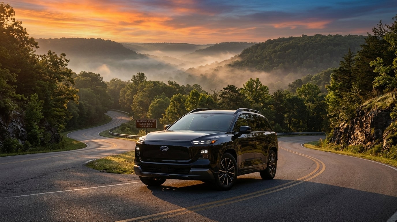 Cinematic wide shot of a futuristic 2027 Subaru Getaway EV traversing a winding mountain pass in the Missouri Ozarks at sunrise, a sleek yet rugged electric SUV with high ground clearance, large all-terrain tires, and a minimalist roof rack, glowing c-shaped LED signature headlights, pearlescent forest green paint catching the warm golden hour light, low-angle perspective emphasizing its capability, mist rising from the valley below, dense oak and pine trees lining the asphalt road, vibrant morning sky with hues of orange and soft blue, photorealistic style, sharp focus on the vehicle's aerodynamic body, high-resolution advertising photography, serene and adventurous mood.