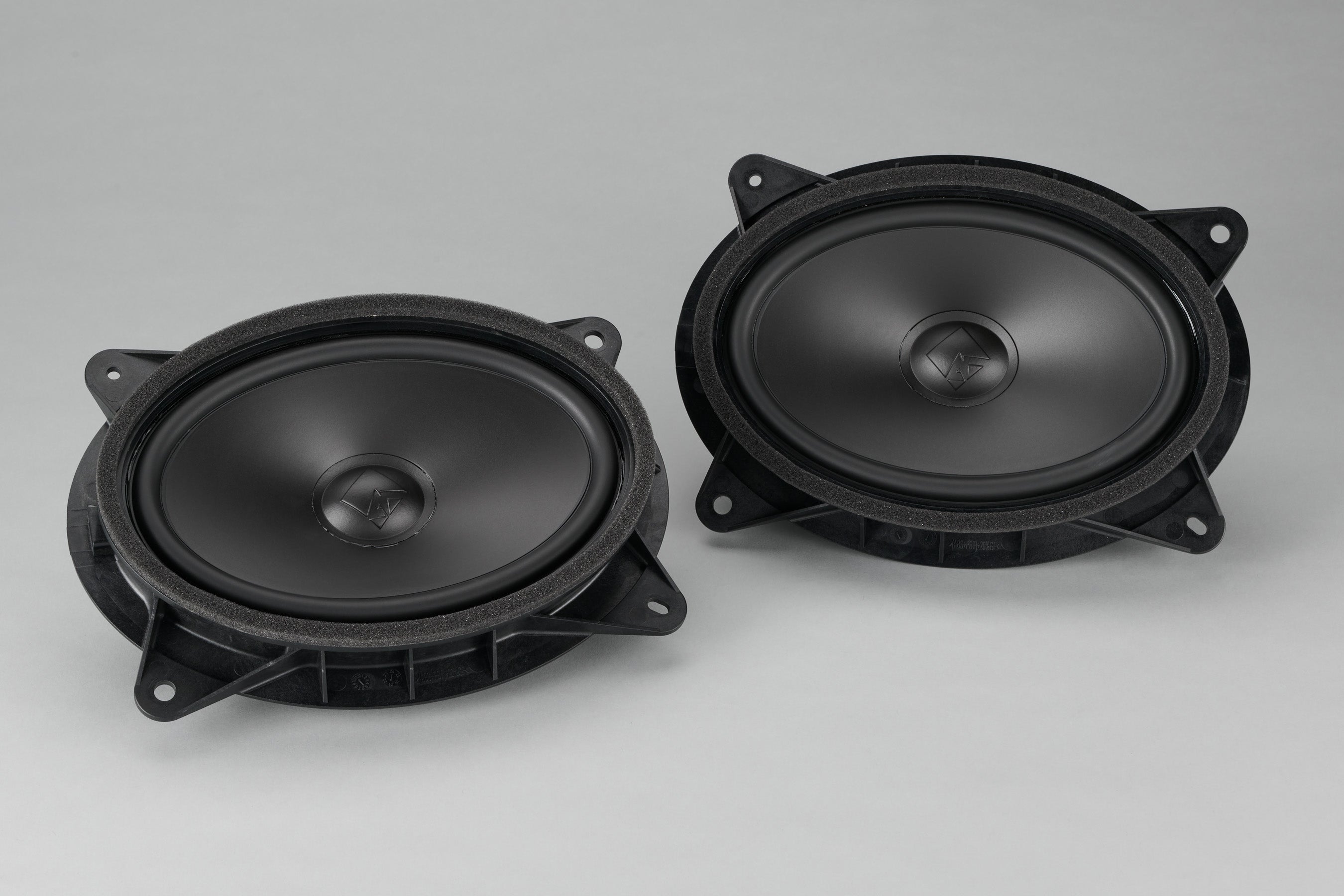 Two black oval car door speakers angled on a grey background.