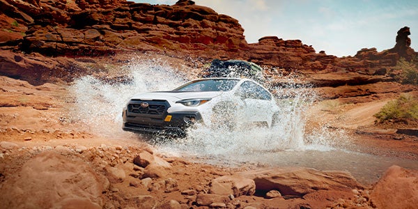 White Subaru Crosstrek Wilderness splashing through a water crossing in a desert canyon.