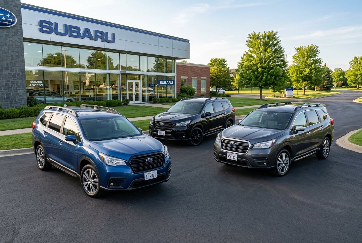Three Subaru Ascent SUVs parked on an asphalt lot in front of a modern Subaru dealership building. (Representative image for illustration purposes only. Actual vehicle may vary based on trim and configuration.)